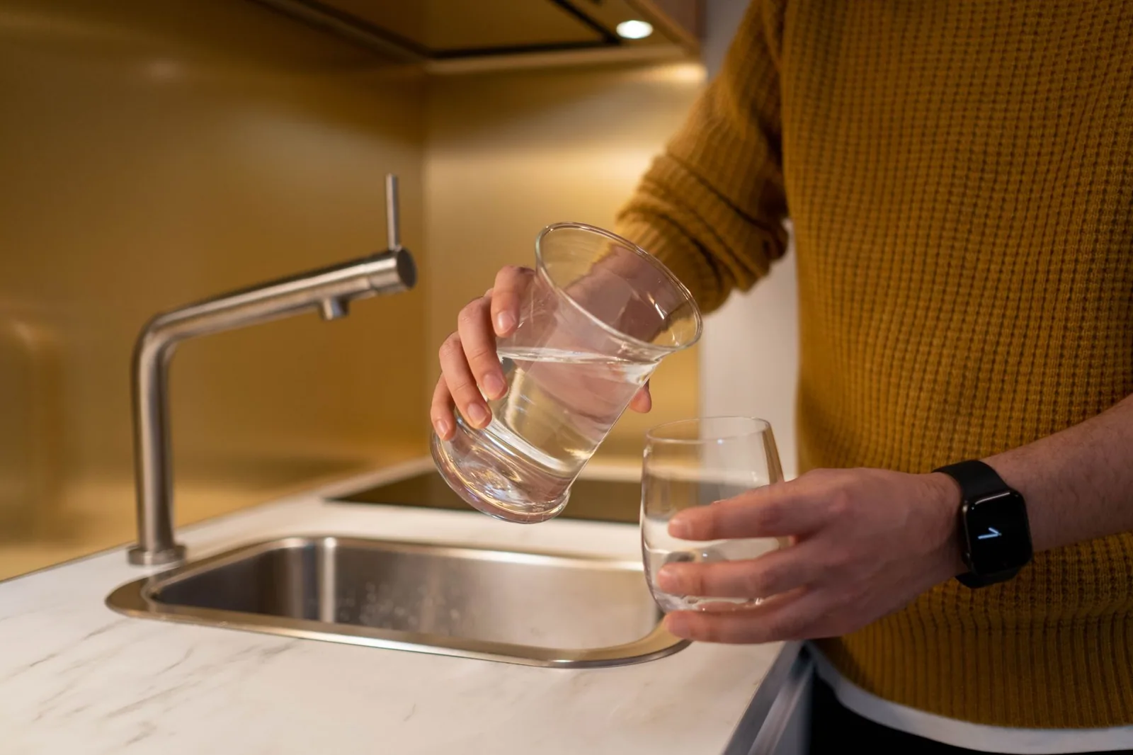 Water poured from a pitcher into a clear glass on a kitchen counter