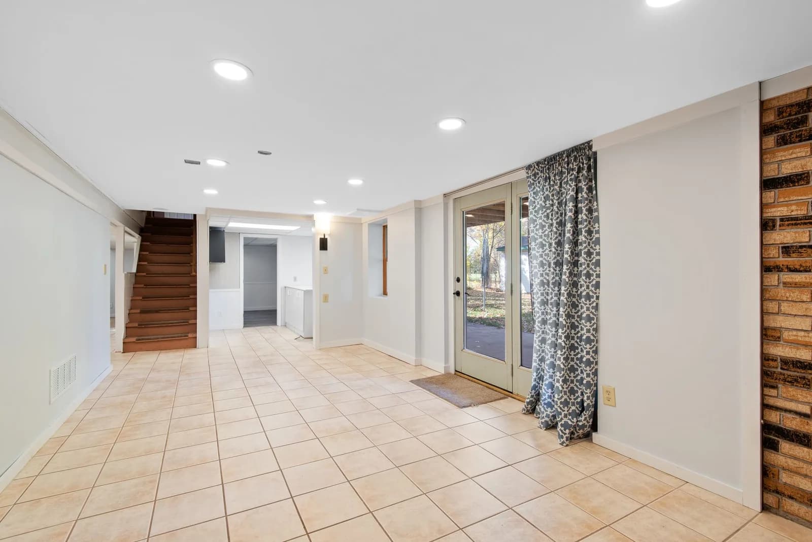 An empty tiled basement room with glass doors to the outside