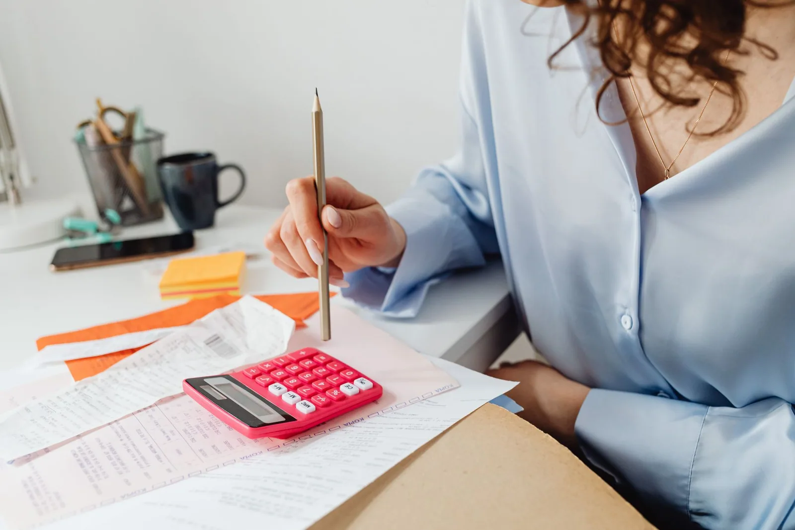 A person adding up monthly expenses with a calculator and a stack of paperwork