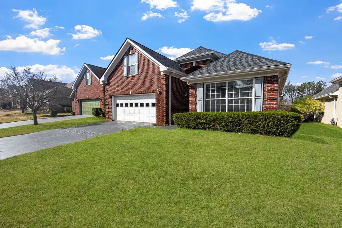 A red brick suburban home with a front lawn under a bright sky