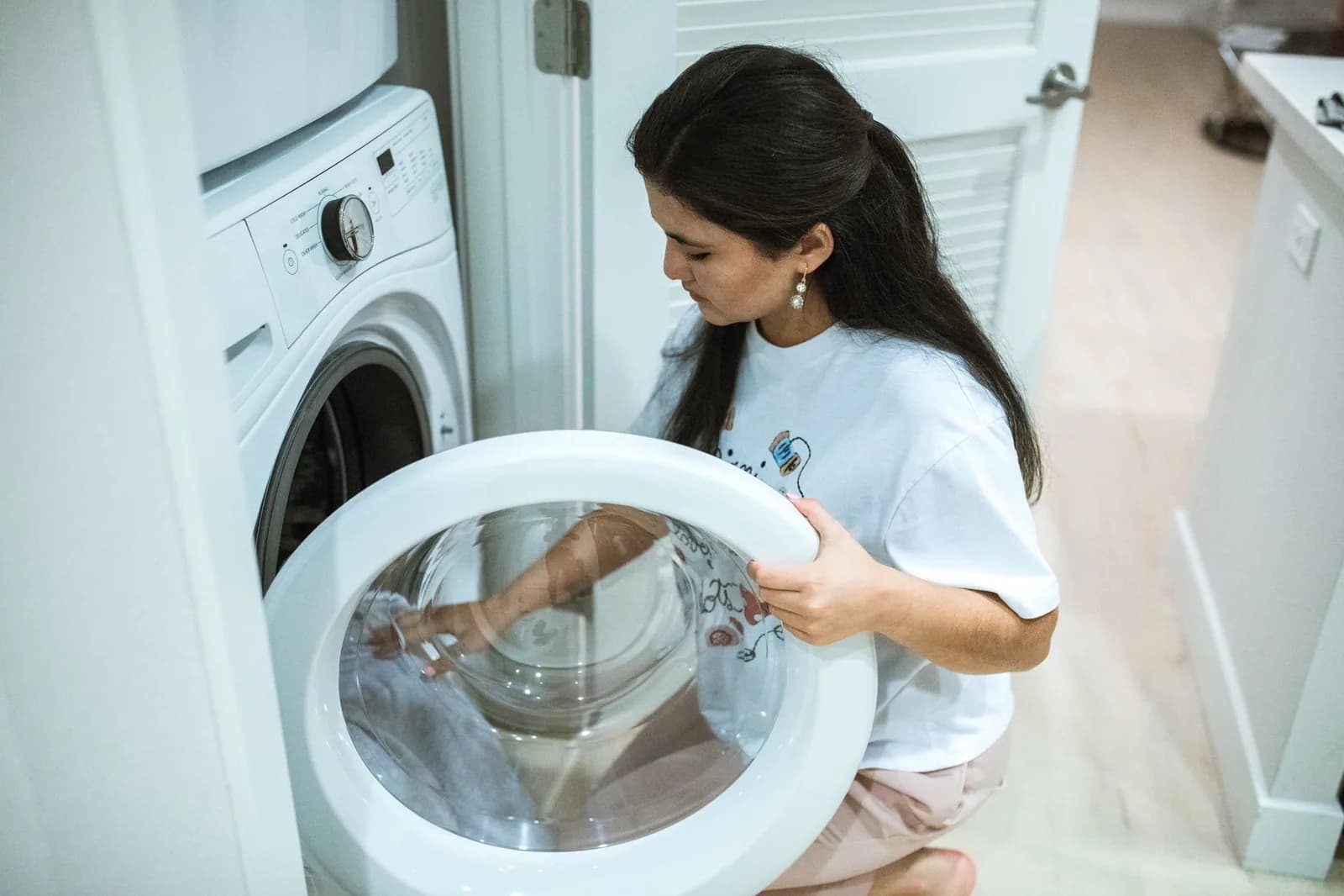 A woman opening the door of a front loading washing machine in a laundry closet