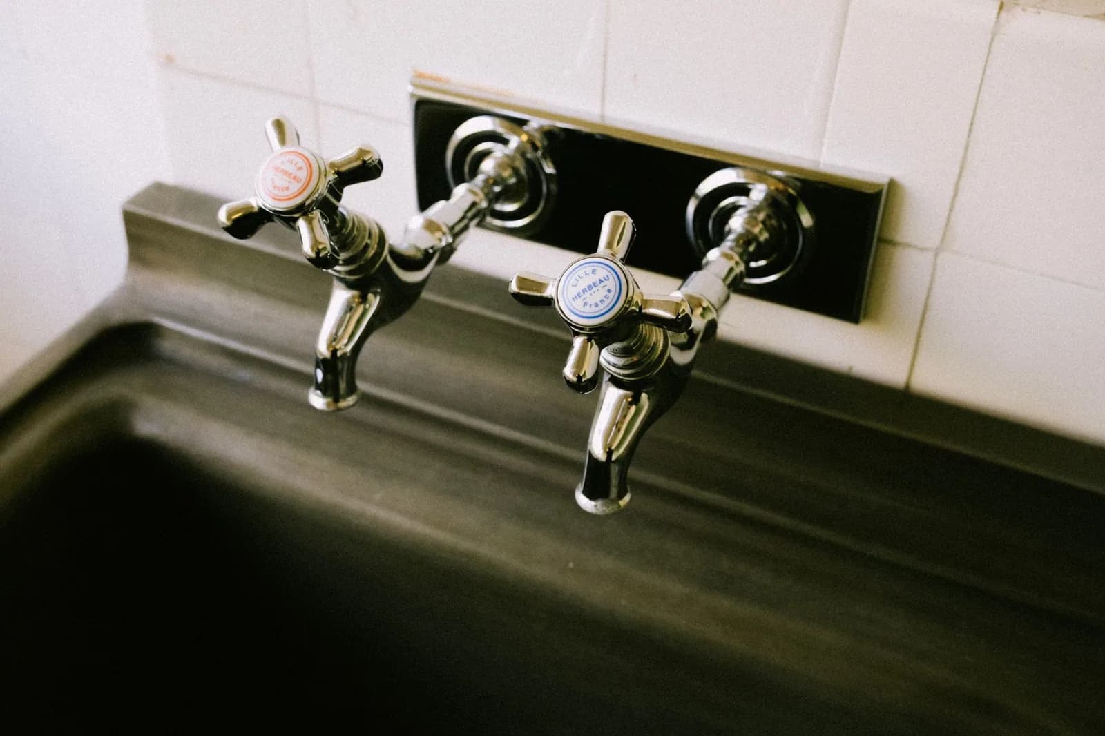 Two chrome cross handle taps above a stainless steel sink in an older kitchen