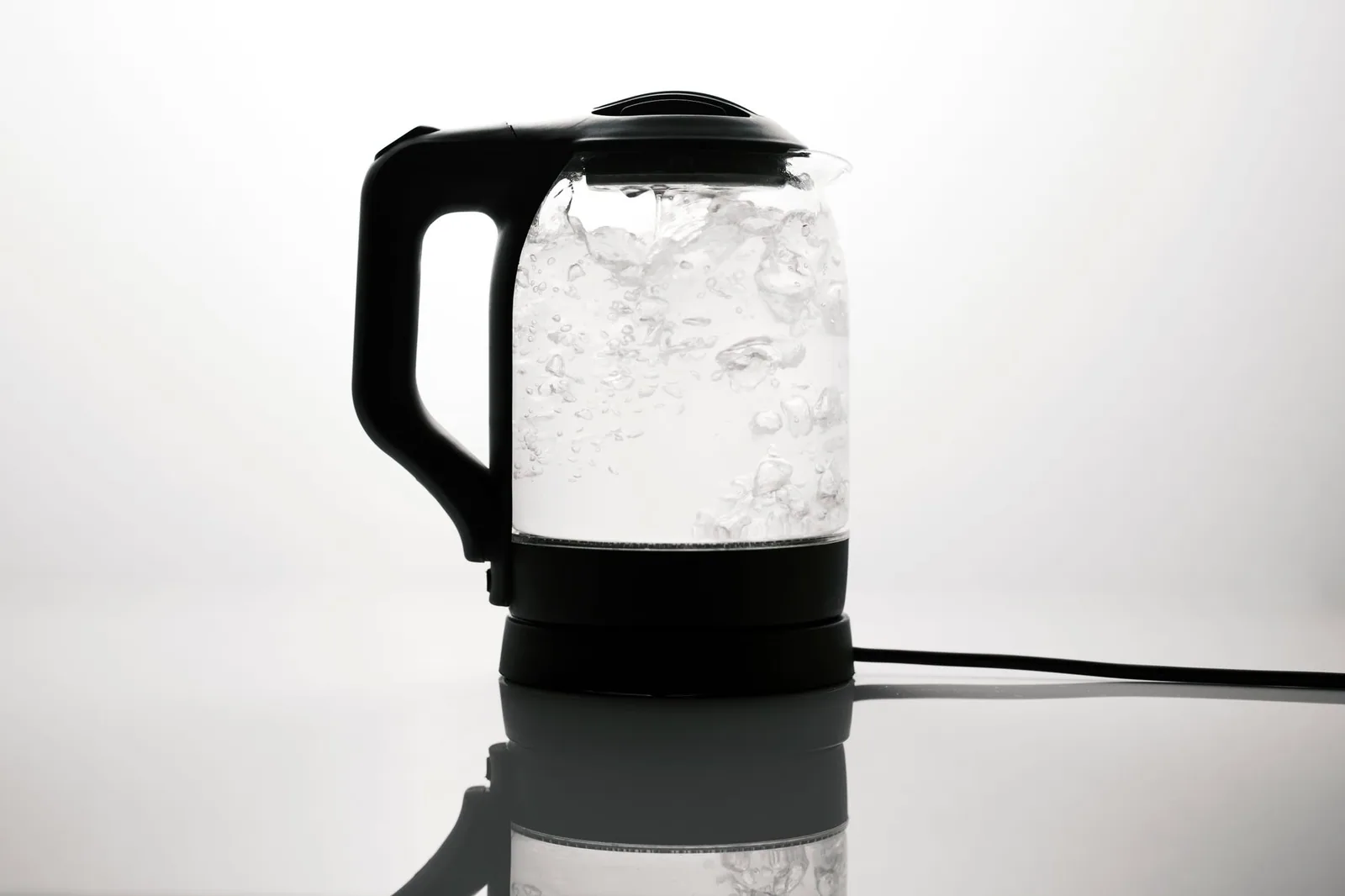 An electric glass kettle at a rolling boil, where hard water leaves its first visible deposit