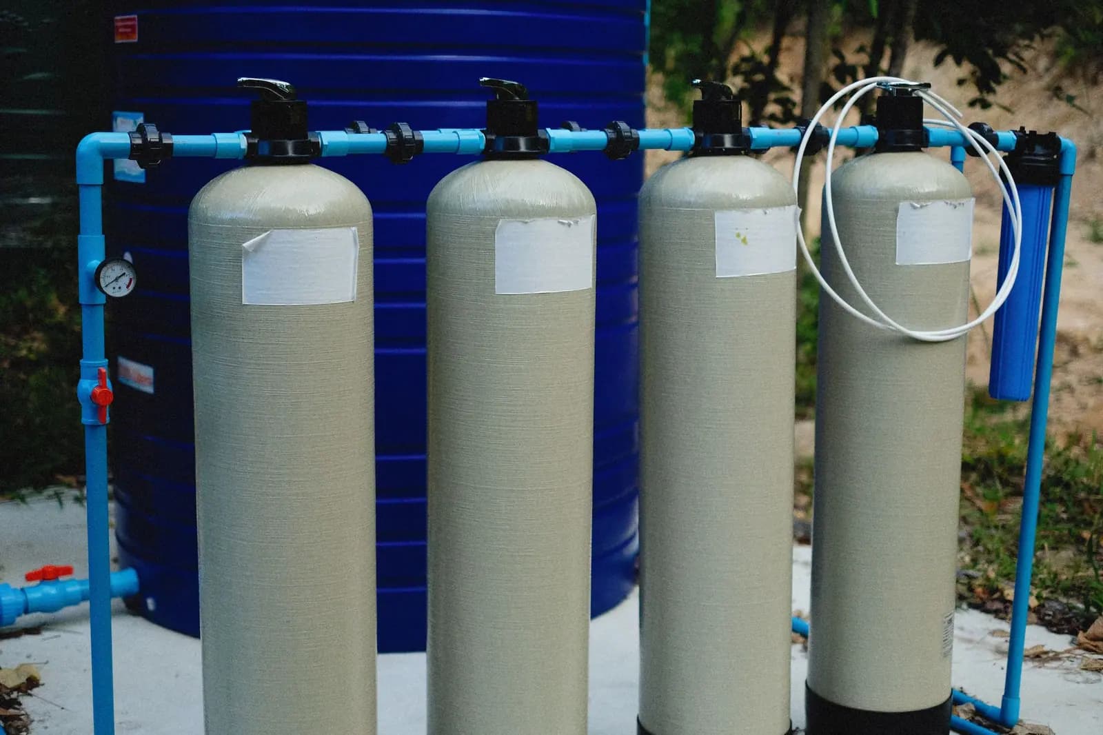 Four fiberglass treatment tanks with control heads, plumbed in series beside a cartridge filter