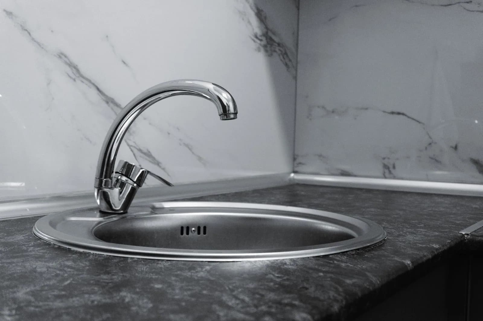 A stainless steel kitchen sink and chrome faucet against a marble backsplash