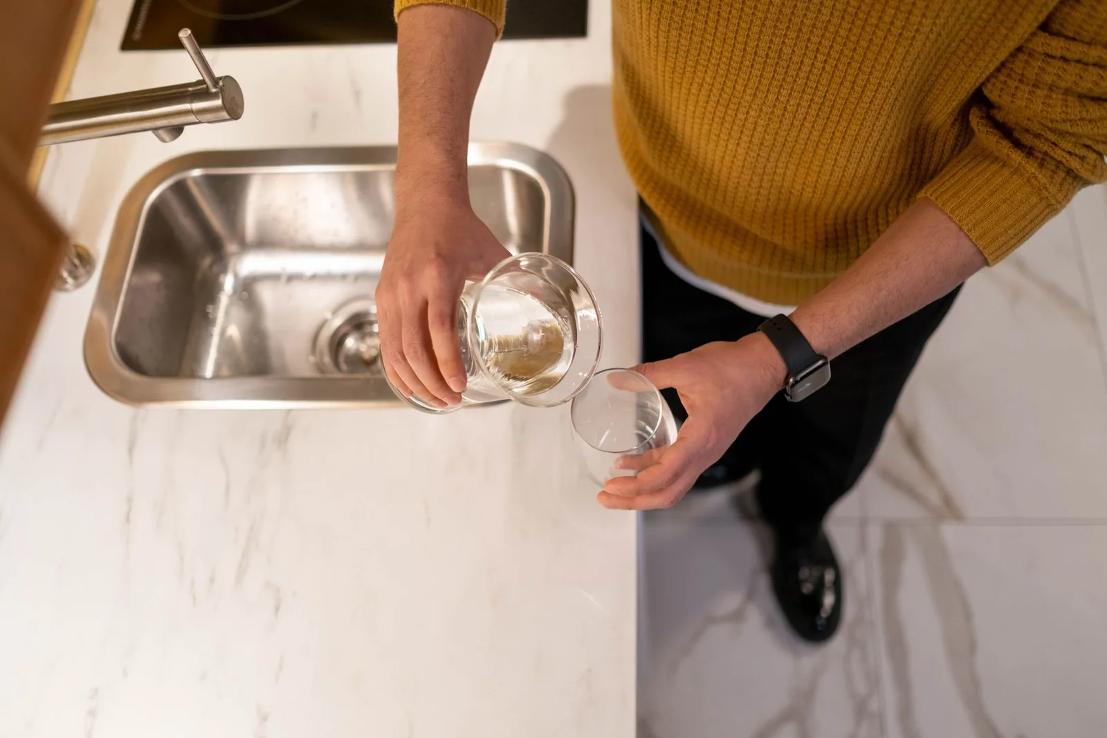 A person filling a drinking glass at a kitchen sink