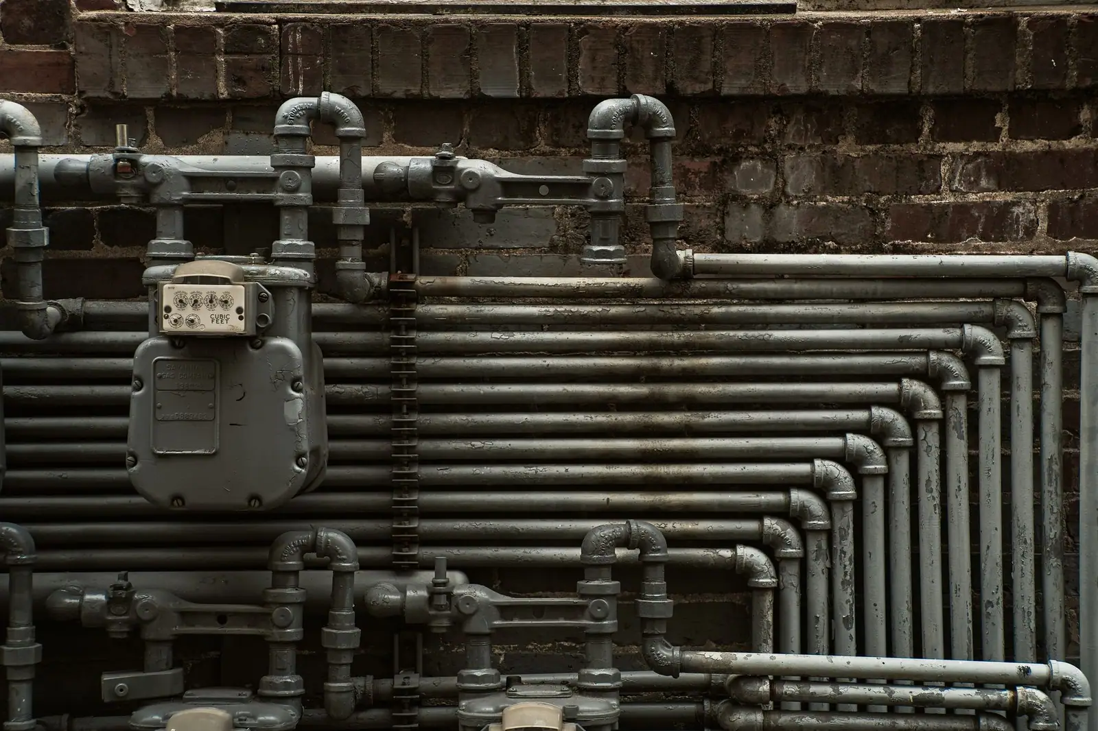 Steel pipes and a meter mounted on a brick wall