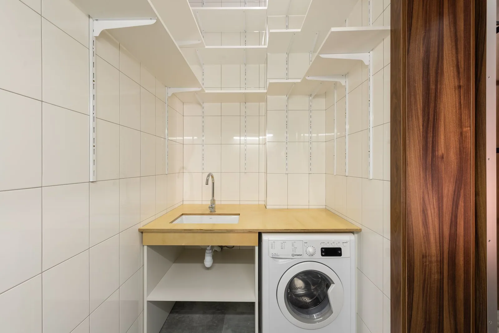 A compact tiled laundry room with a washing machine tucked under the counter