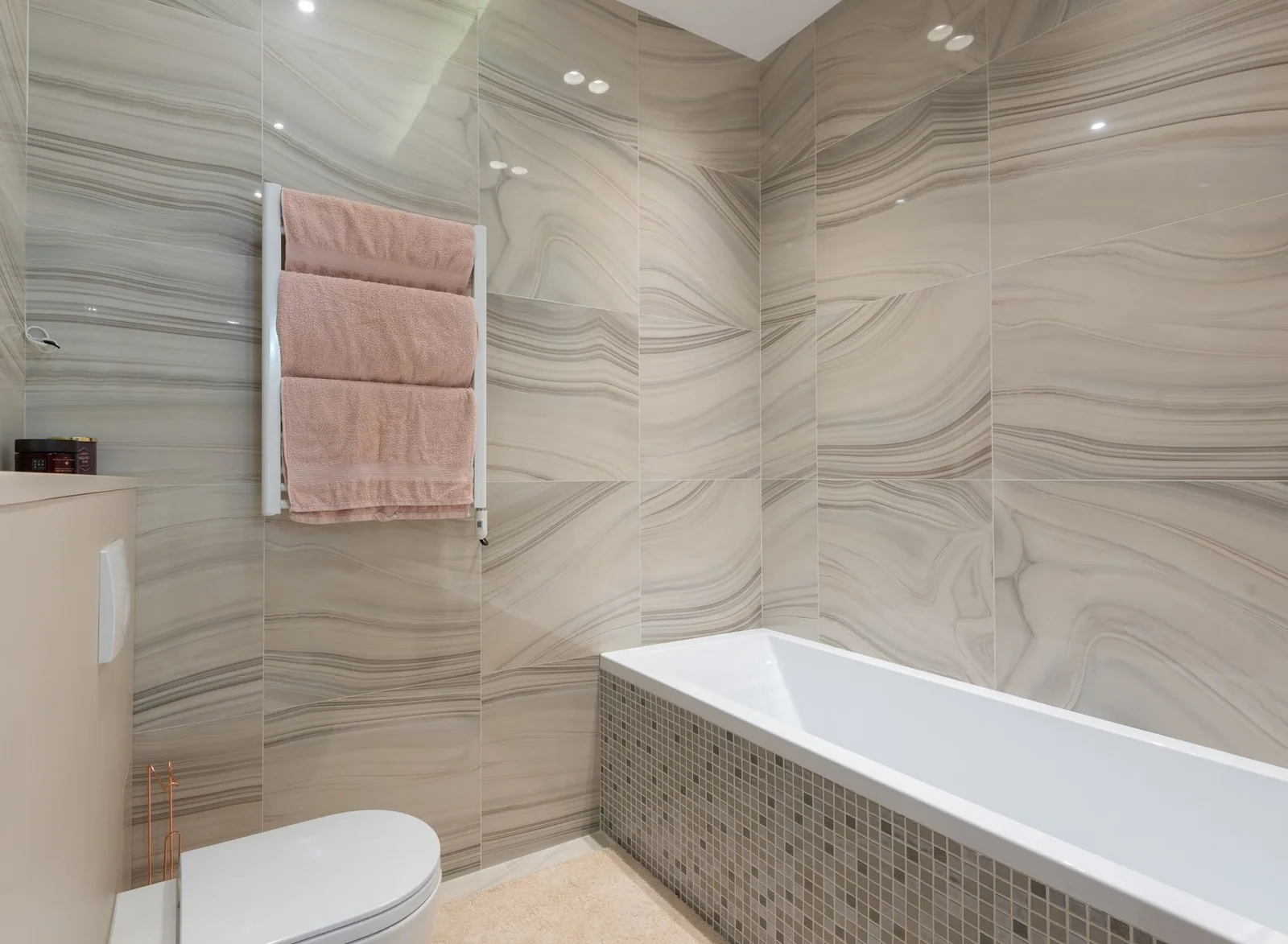 A tiled bathroom with a built in bath and a heated towel rail