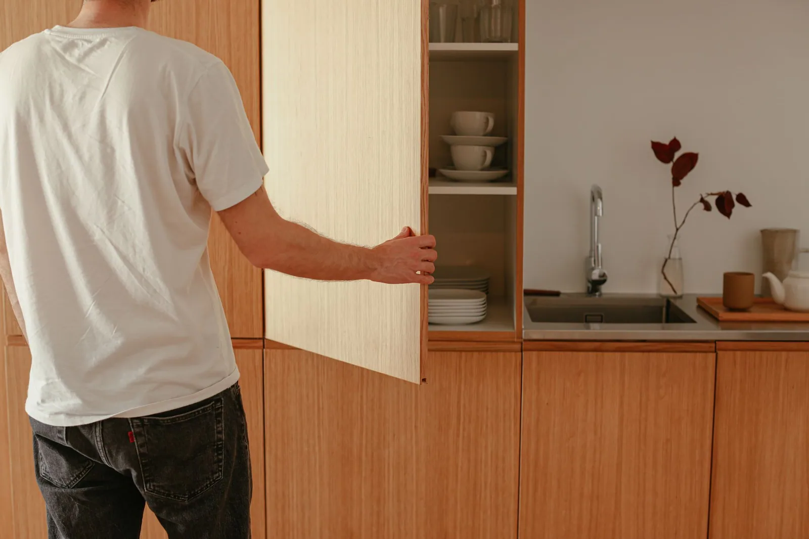 Someone opening a cabinet in a fitted kitchen, where the run under the sink hides whatever is plumbed in