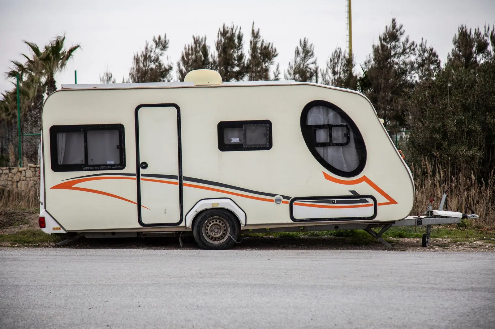 A white travel trailer parked outdoors with its door side facing an open pitch