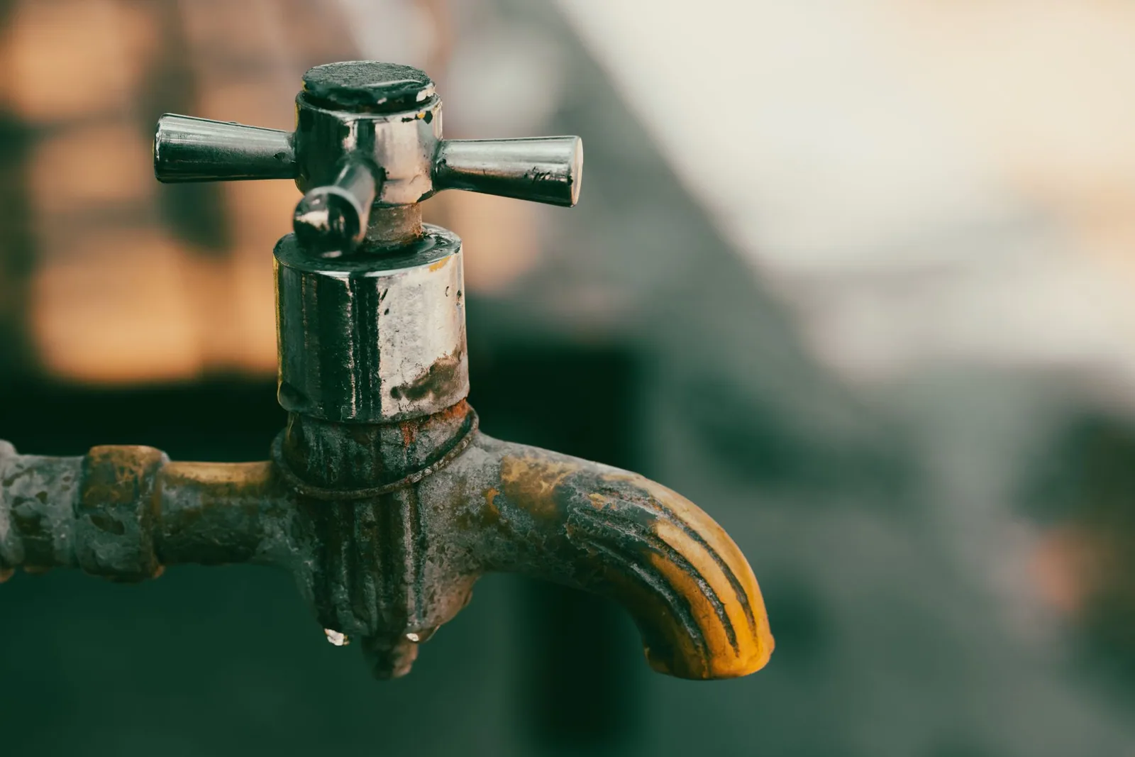 Water droplets on an old metal faucet with a worn, crusted finish