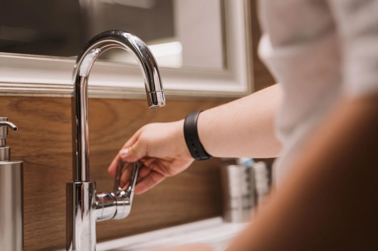A hand turning the handle of a chrome faucet