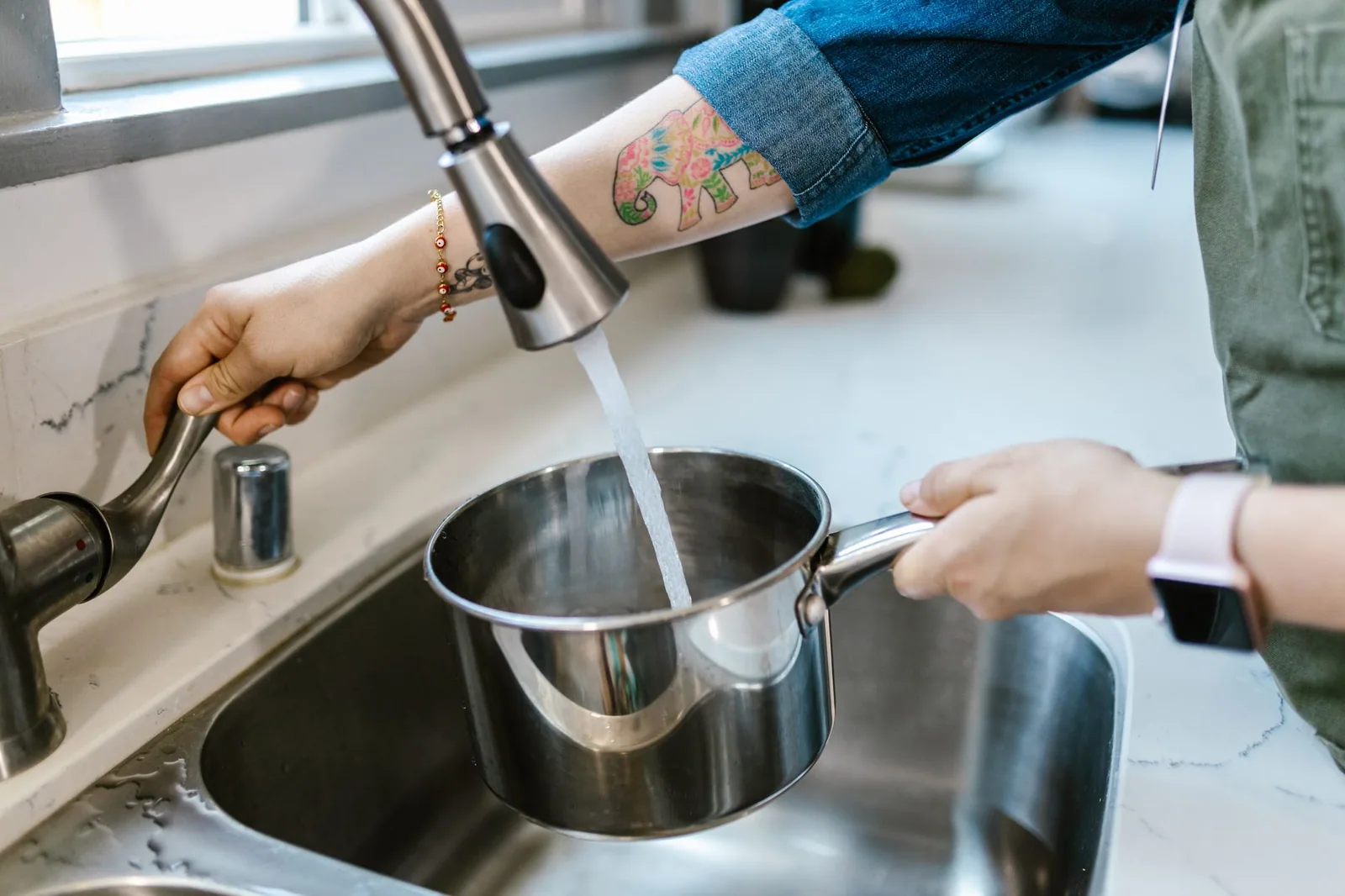 Hands holding a pot under a kitchen tap as it fills with water