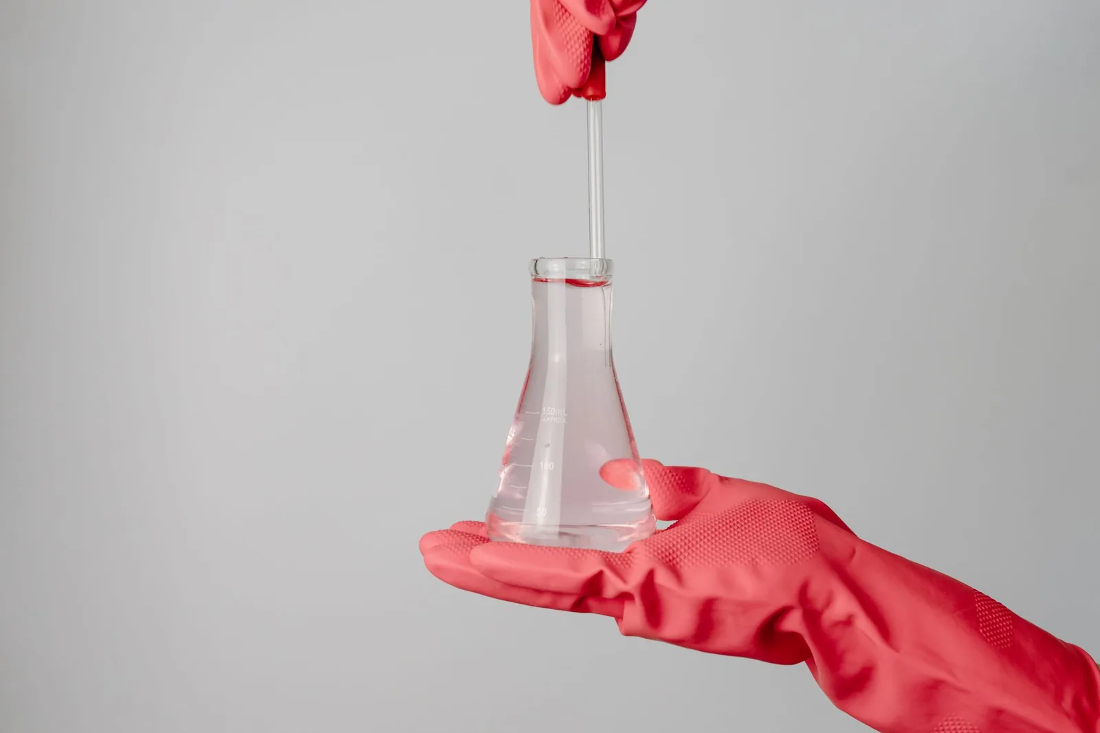 Gloved hands holding a laboratory flask of clear water sample up to the light