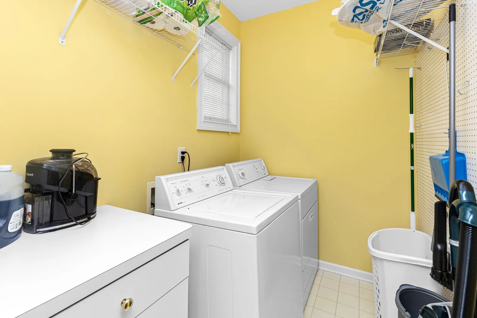 A bright laundry room with a washer, a dryer and open shelving