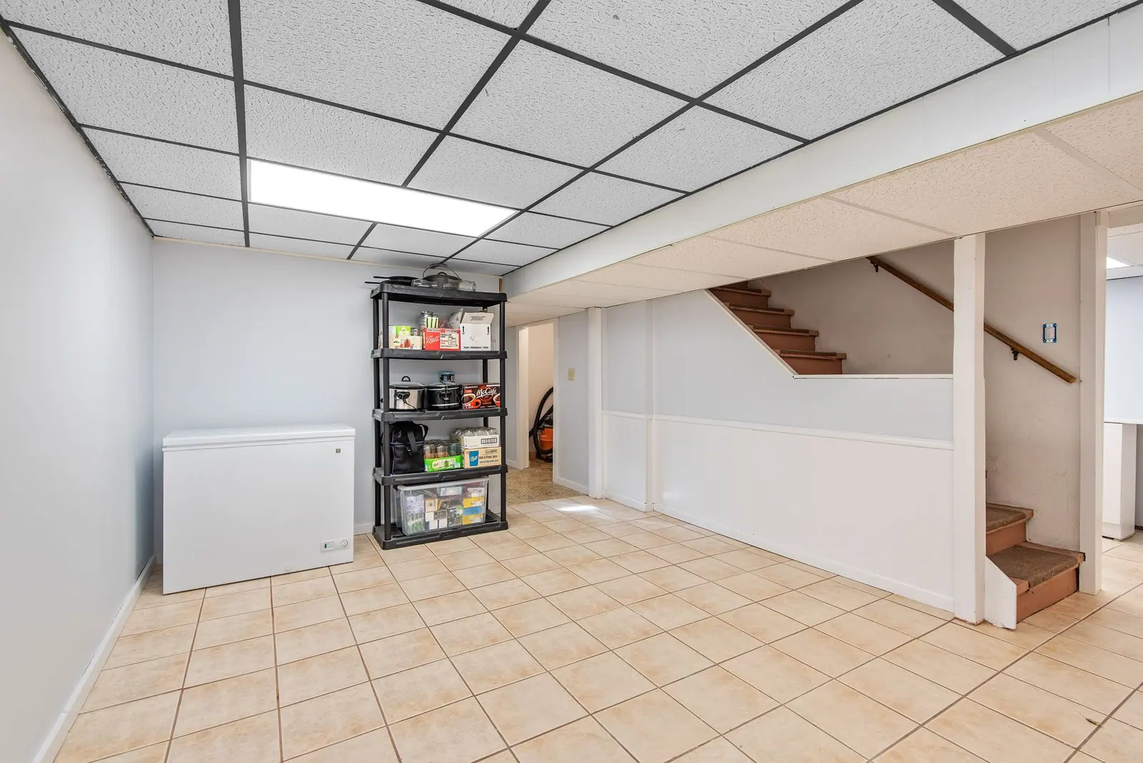 An empty basement with storage shelving and a staircase, the usual spot for a softener