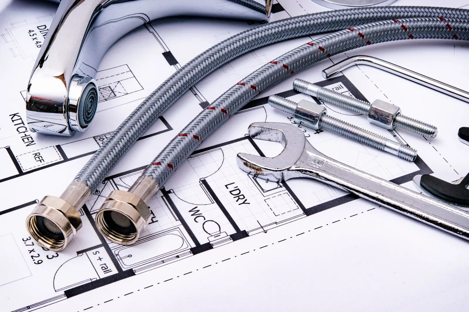 A wrench, pipe fittings and a faucet laid out on a printed blueprint
