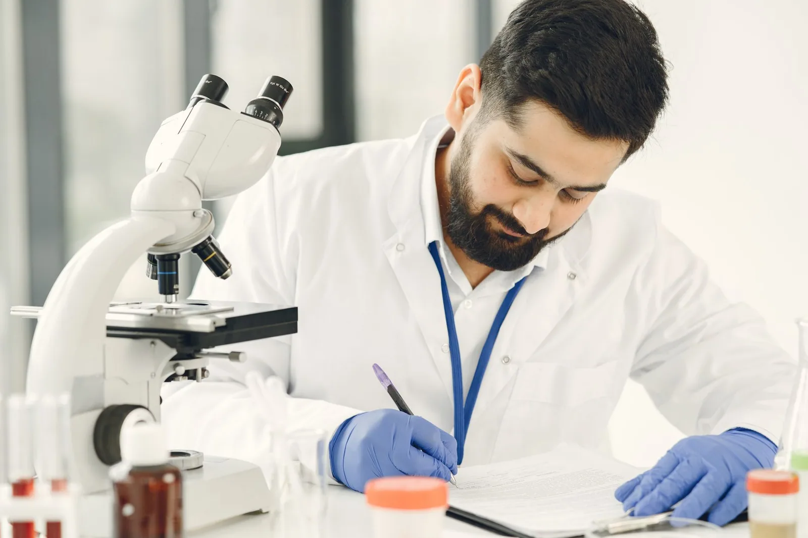 A lab technician writing notes beside a microscope