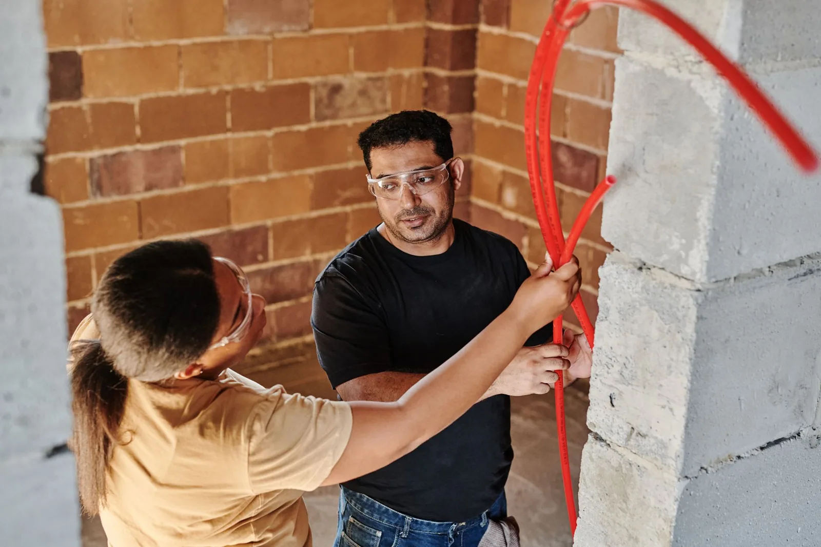 Two installers fitting tubing along a brick wall