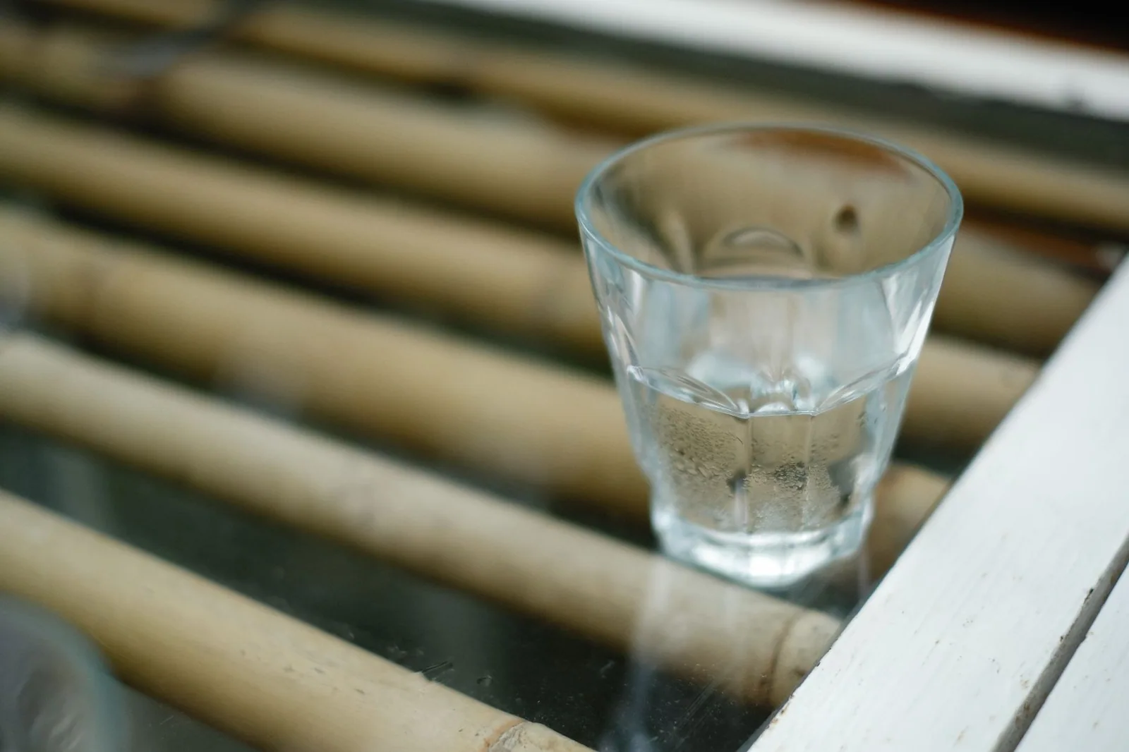 A short glass of clear tap water on a glass table by a window
