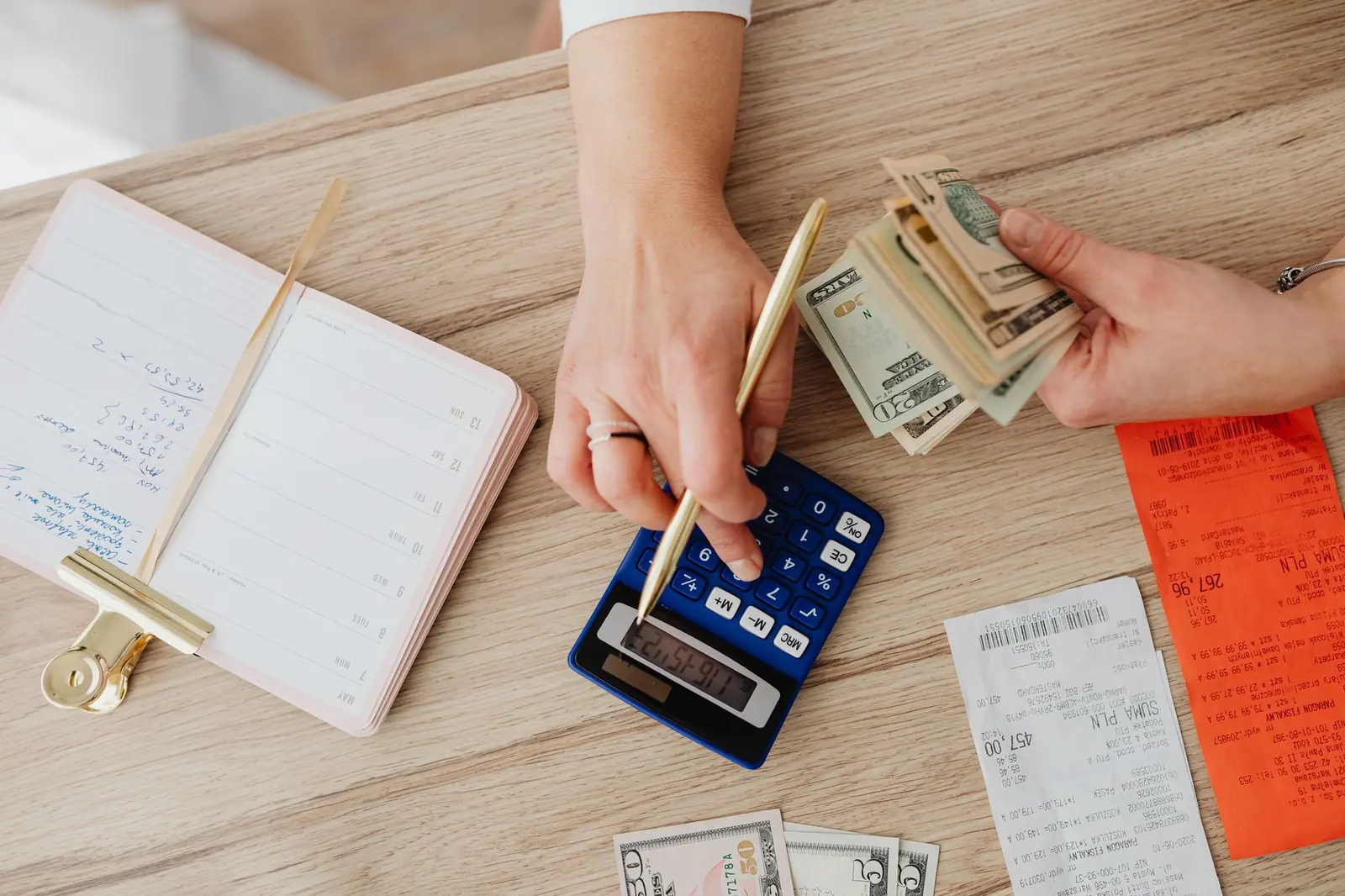 Hands working a calculator over cash and receipts on a wooden table