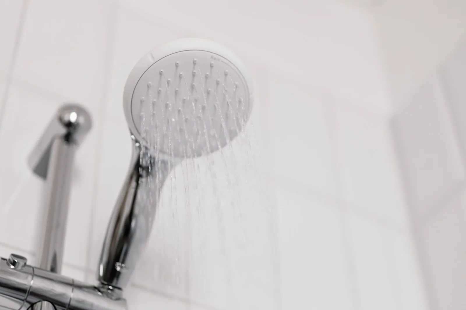 A shower head running at full flow against white bathroom tiles