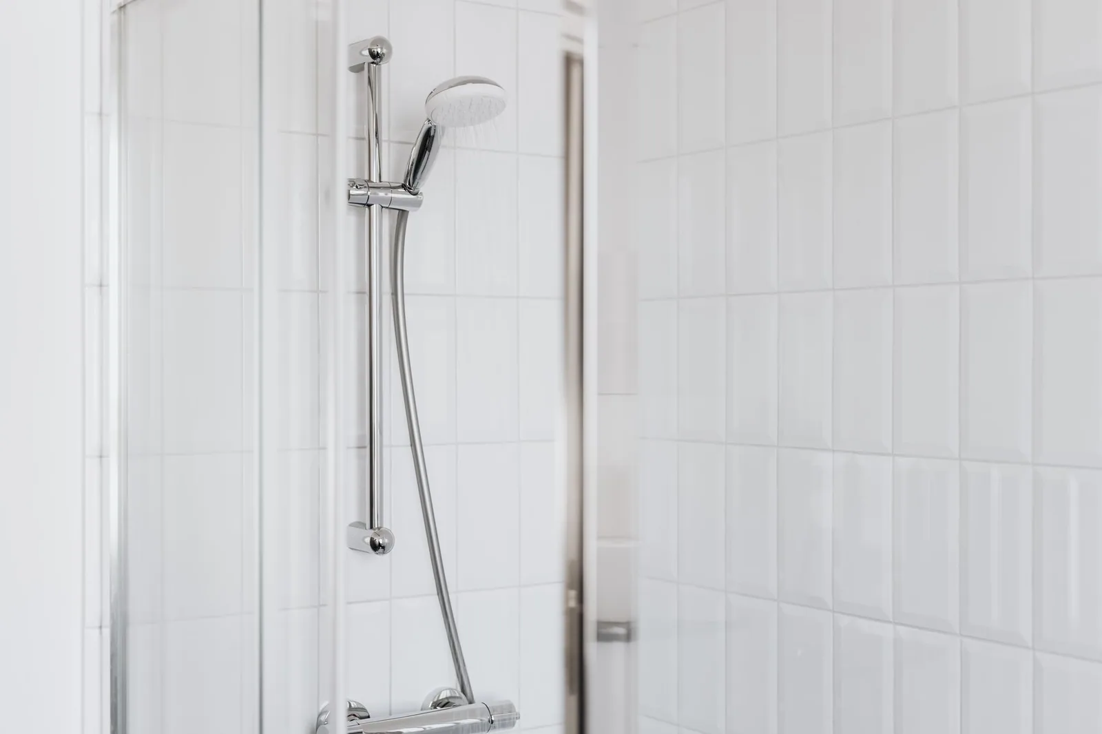 A chrome shower head and fixtures against clean white bathroom tiles