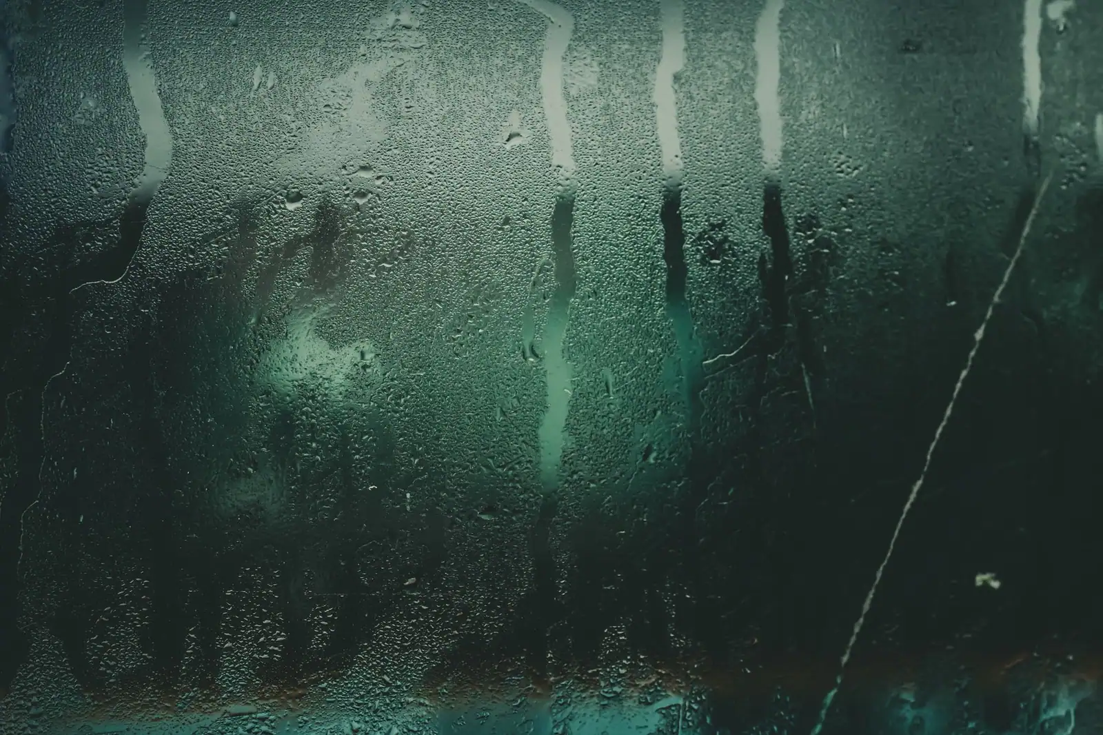 Water droplets and streaks running down a fogged glass panel