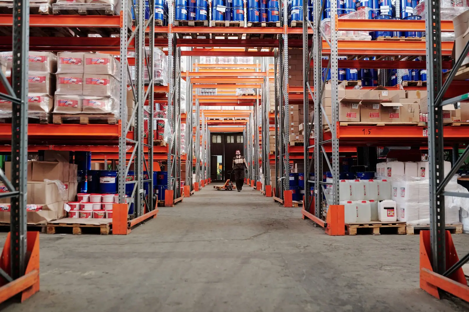 A worker in a warehouse aisle lined with stocked shelves