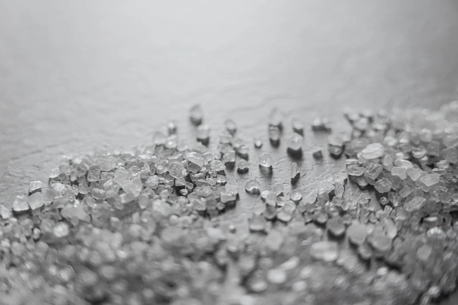 Coarse rock salt crystals scattered across a dark surface