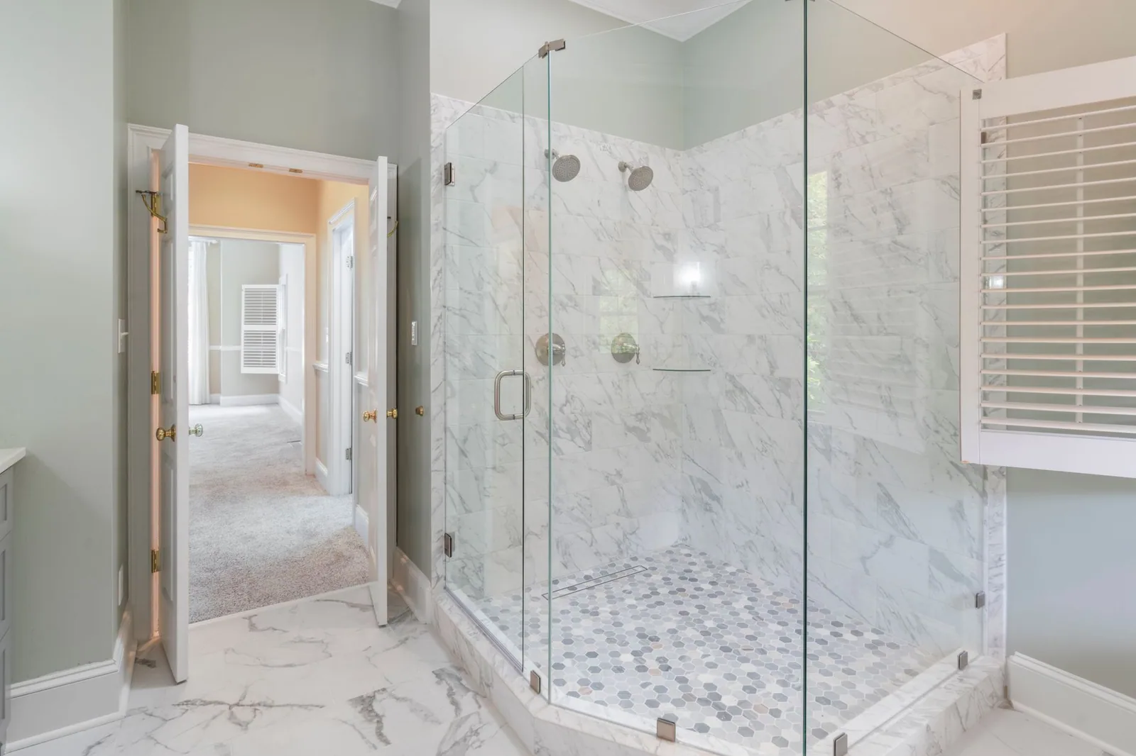A clear glass shower enclosure in a marble tiled bathroom