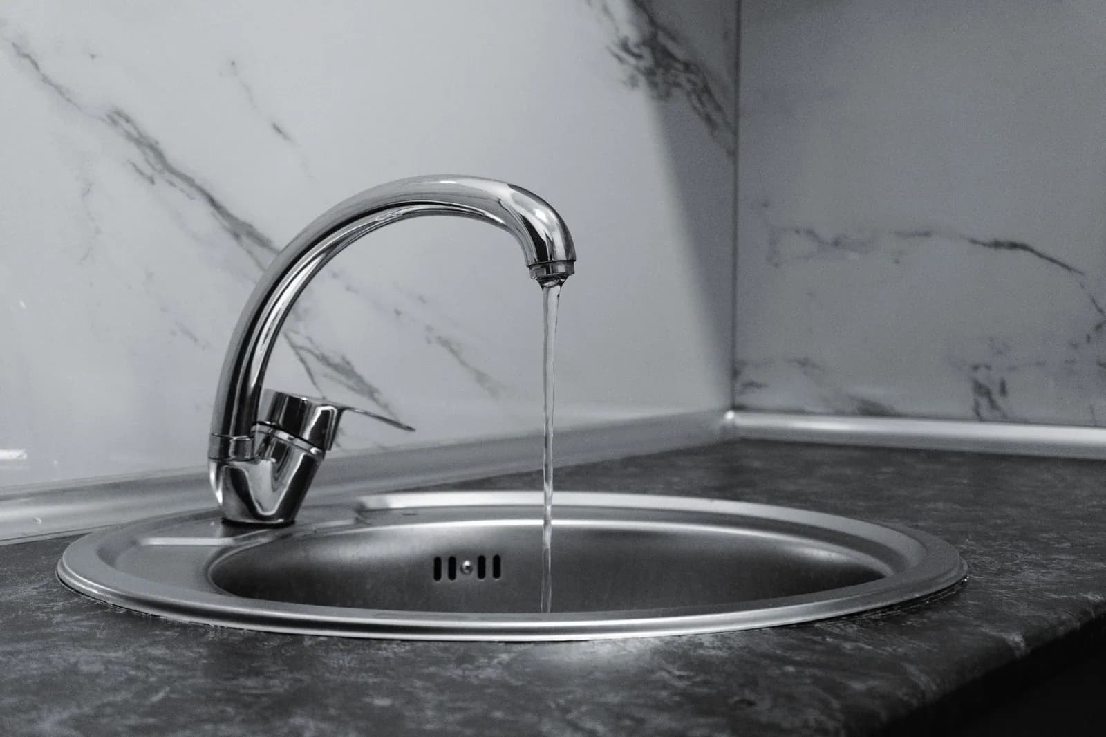 Water running from a chrome kitchen faucet into a stainless steel sink