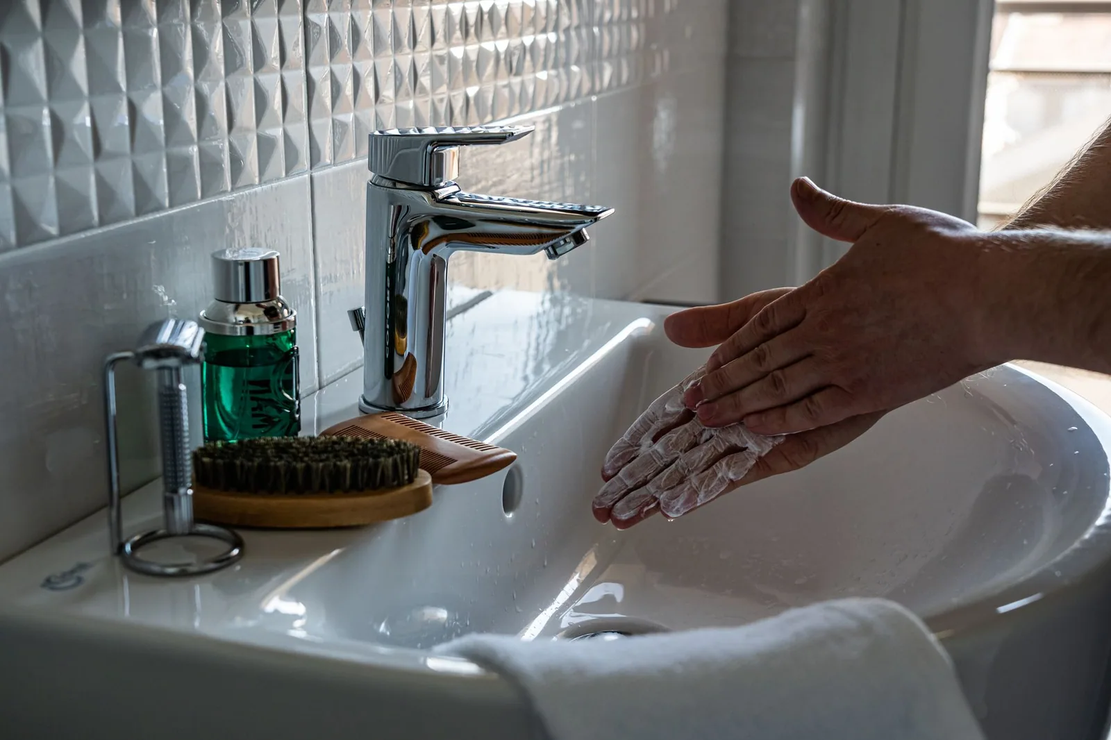 Hands working up a soap lather under a running bathroom tap